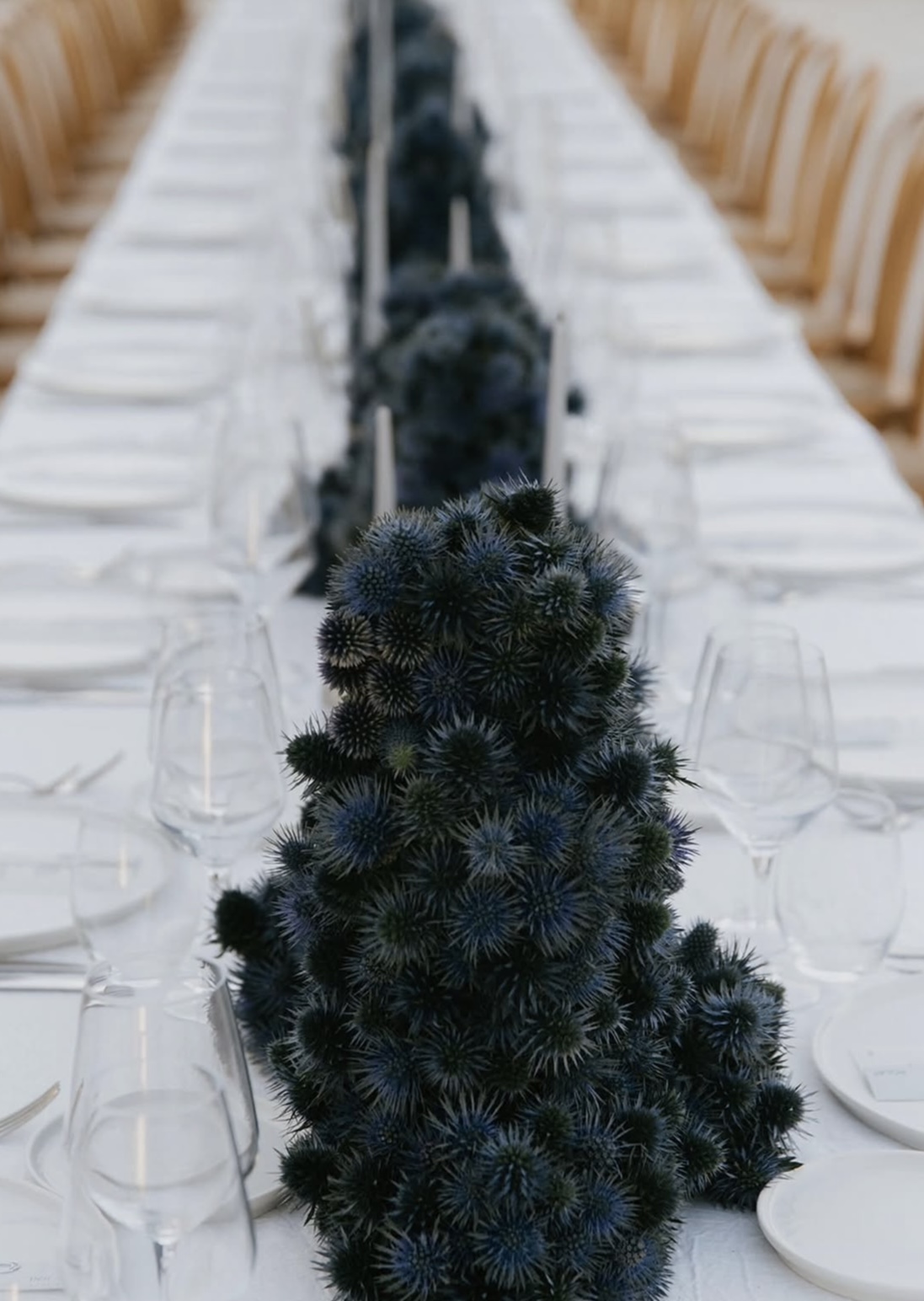 Sculptural dark thistle centerpiece along a long candlelit table
